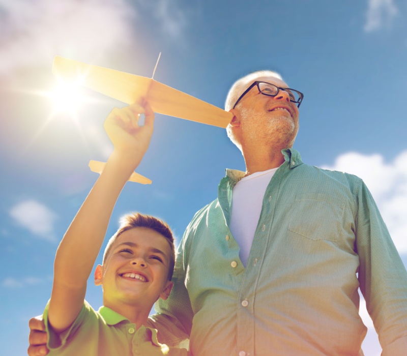 A grandfather and grandson playing with a toy plane outdoors.