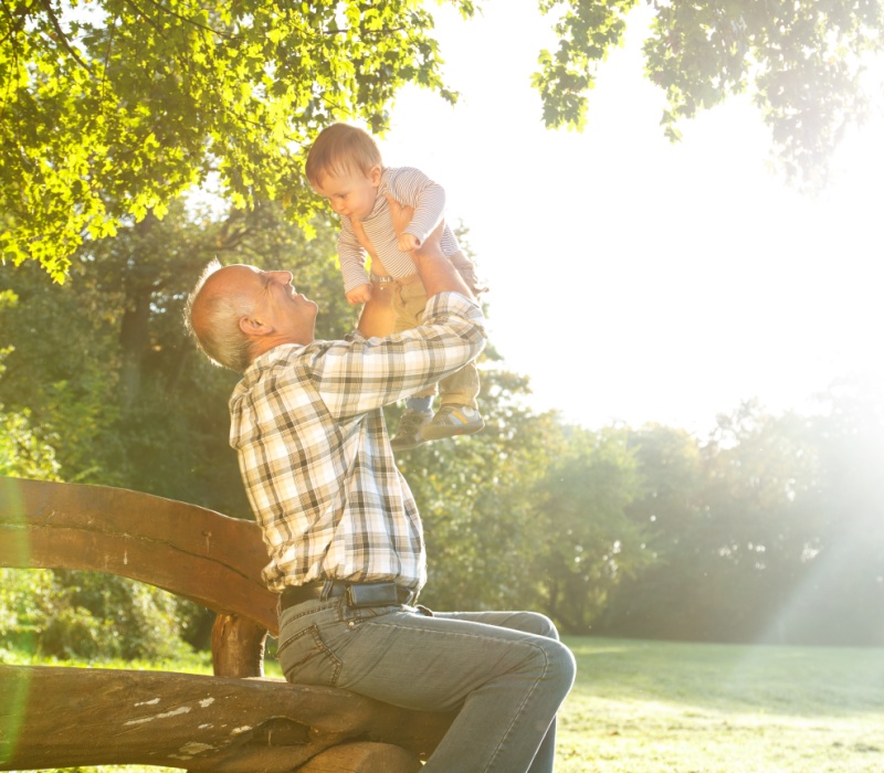 A grandfather playing with his young grandson in a park.